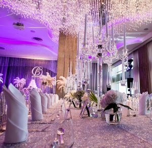 Lavish indoor wedding reception designed by Tiffany Siegel with a breathtaking ceiling of cascading crystal lights, mirrored tables reflecting elegant candelabras, and plush white floral arrangements, creating a luxurious and romantic atmosphere.