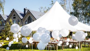 Magical outdoor event designed by Tiffany Siegel, featuring a constellation of varying sized white balloons soaring above banquet tables, under a grand peaked tent, adding a touch of whimsy to the sophisticated outdoor celebration space.