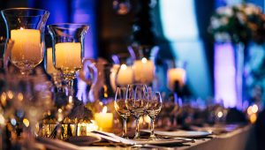 Intimate and elegant table setting for an event designed by Tiffany Siegel, featuring glowing candles in tall glass holders and crystal wine glasses, all set against a backdrop of soft, ambient lighting for a warm and inviting dining experience.