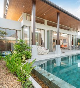 Modern outdoor oasis designed by Tiffany Siegel, featuring a sleek infinity pool surrounded by lush landscaping, with a chic hanging chair and striking architectural details of the home providing a luxurious space for relaxation and entertainment.