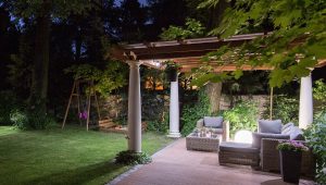 Tranquil backyard patio retreat designed by Tiffany Siegel, featuring a cozy outdoor lounge area with plush seating and a woven wicker coffee table under a vine-covered pergola, inviting relaxation in a serene garden setting.