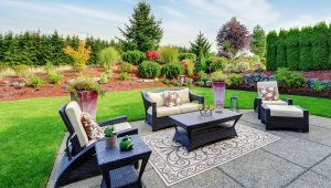 Vibrant garden landscape with a stylish outdoor seating arrangement by Tiffany Siegel, featuring elegant dark rattan furniture with comfortable cushions, set on a patterned outdoor rug, all complemented by a colorful, manicured garden in full bloom.