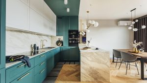Contemporary kitchen designed by Tiffany Siegel, featuring striking teal cabinetry, elegant marble backsplash and island countertop, complemented by gold hardware and sophisticated globe pendant lights, harmoniously paired with a warm wooden dining area.