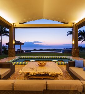 Covered outdoor lounge with a sunken sofa facing the ocean at dusk