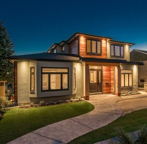 Two-story contemporary home with wood and stucco siding, lit at dusk above a curved walkway